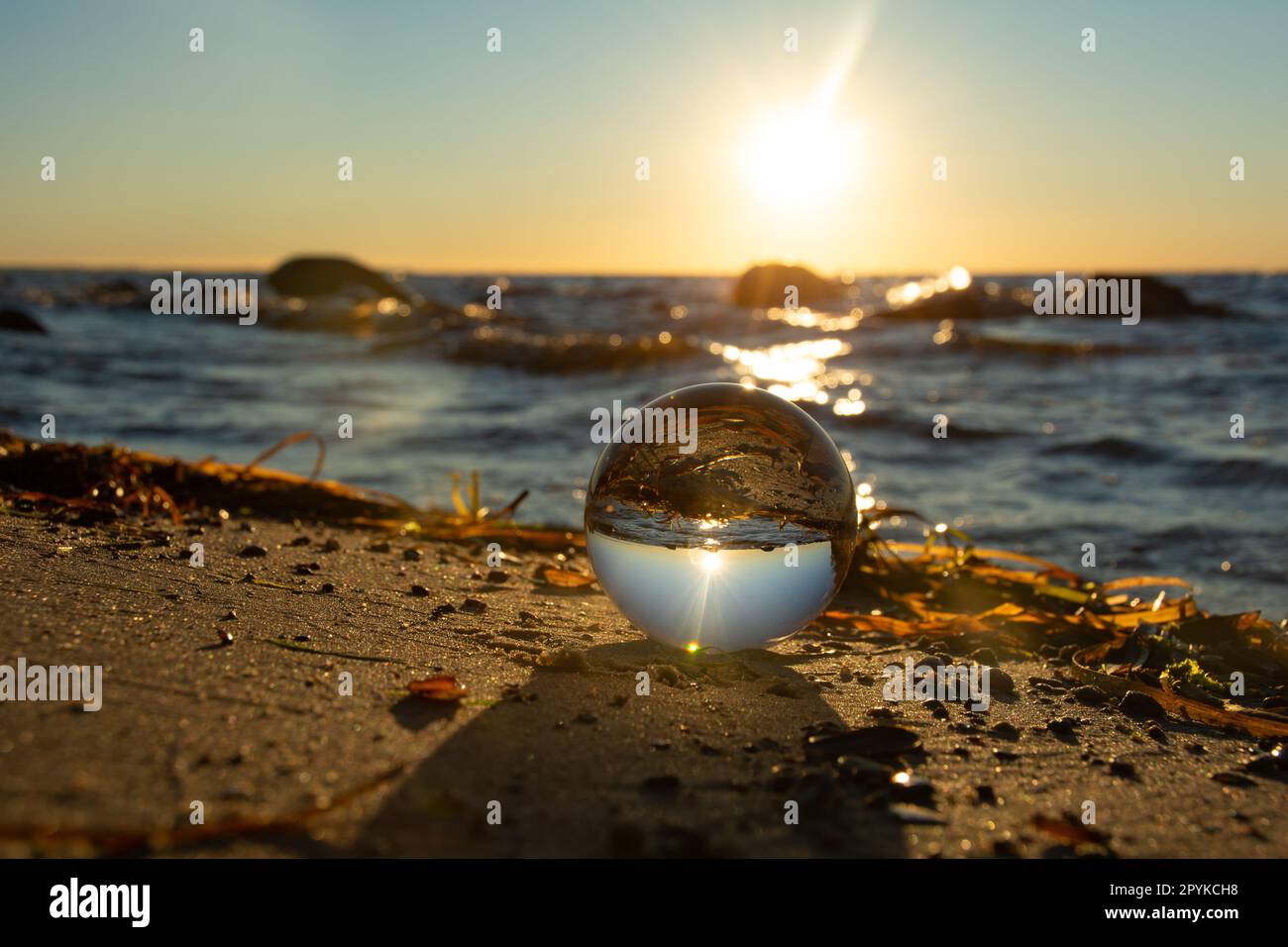 La plage et la mer se reflètent dans une sphère couchée dans le sable Banque D'Images