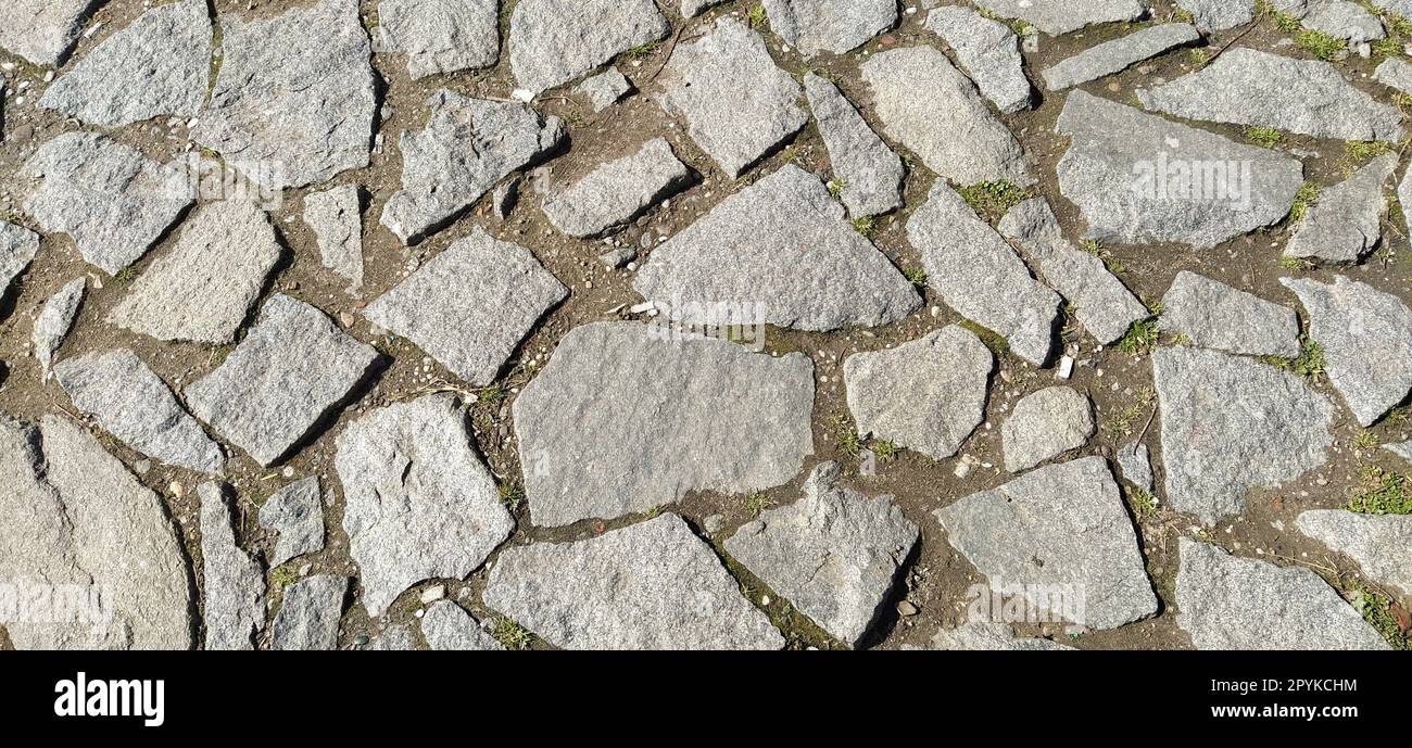 chaussée pavée de pierres grises et brunes naturelles inégales. Entre les pavés broyés, il y a de petits cailloux, de la terre, du sable, de l'herbe. Éclairage solaire. Place dans la vieille ville européenne Banque D'Images