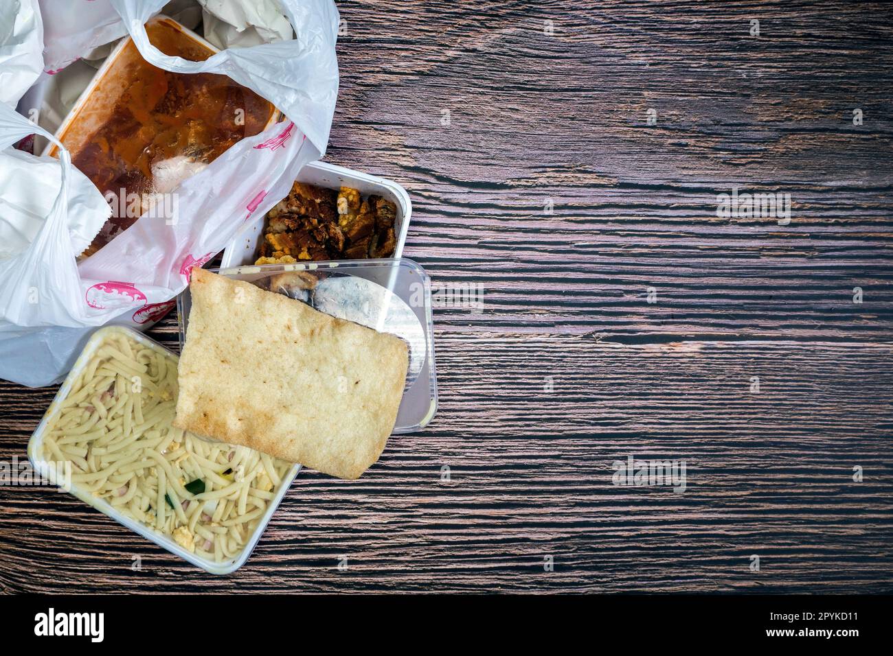 Sélection de plats chinois à emporter dans un sac en plastique. Bami, babi pangang, bœuf haché croustillant, poulet aigre-doux, vue de dessus krupuk sur l'espace de copie de table en bois. Livraison de nourriture Banque D'Images