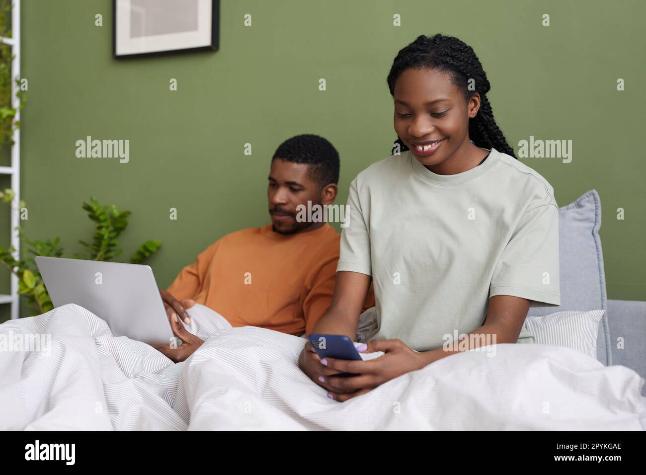 Jeune couple afro-américain utilisant des gadgets tout en se reposant au lit pendant le week-end à la maison Banque D'Images