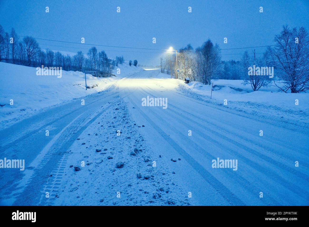 Paysage d'hiver en Scandinavie. Route enneigée avec arbres enneigés. Sur la route illumine un feu de rue. Photo de paysage du nord Banque D'Images