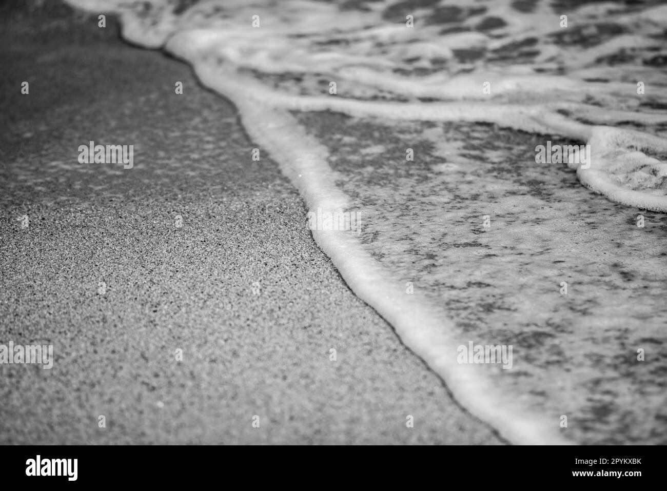 L'océan se déforme avec de la mousse sur une plage de sable Banque D'Images
