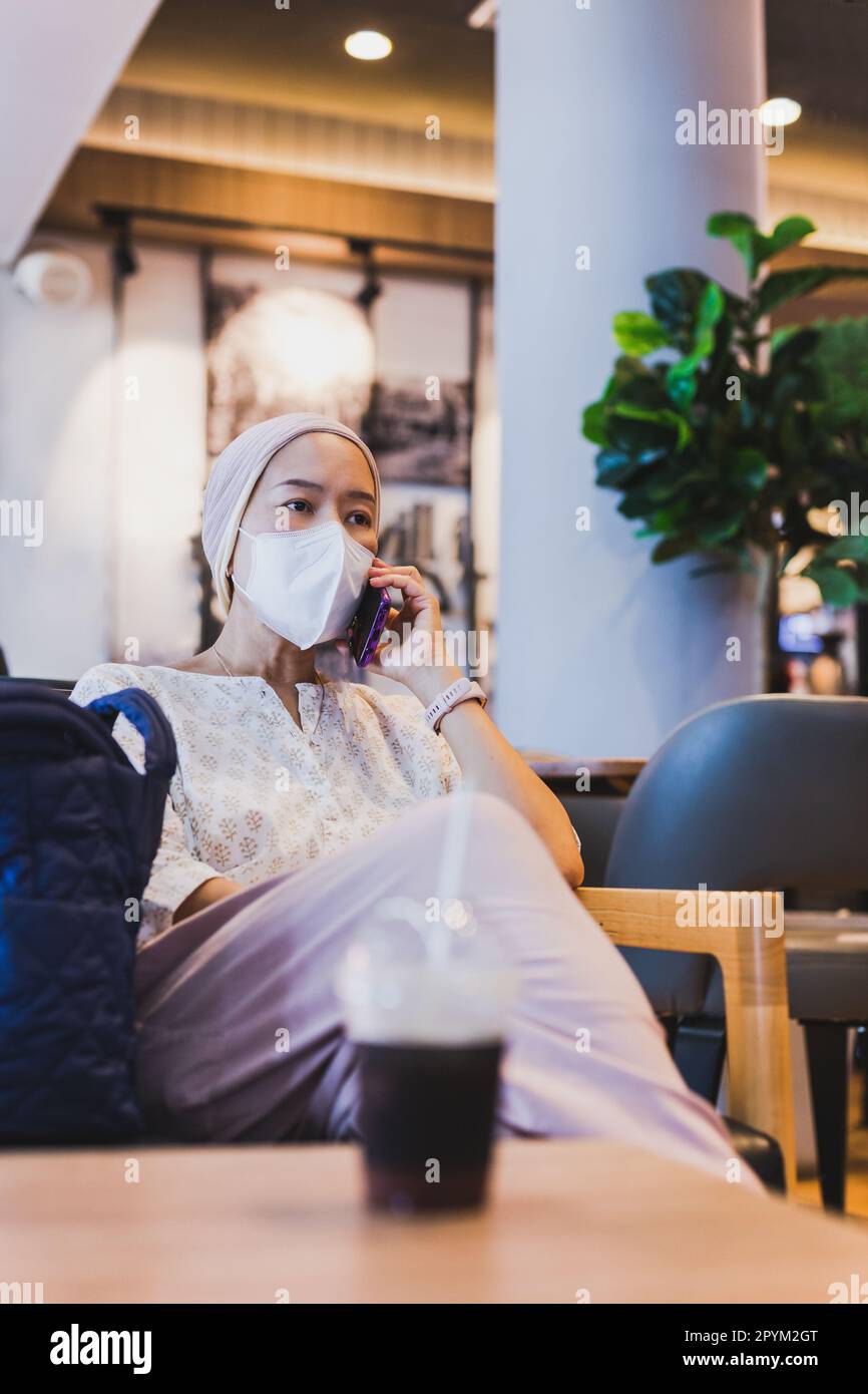 Femme portant un masque facial de protection parlant sur un téléphone portable dans un café. Banque D'Images