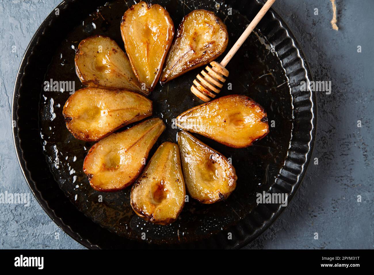 Poires cuites au miel, vinaigrette Modena et cannelle, et une immersion au miel dans une plaque de cuisson ronde sur fond de cocotte bleu grisâtre Banque D'Images