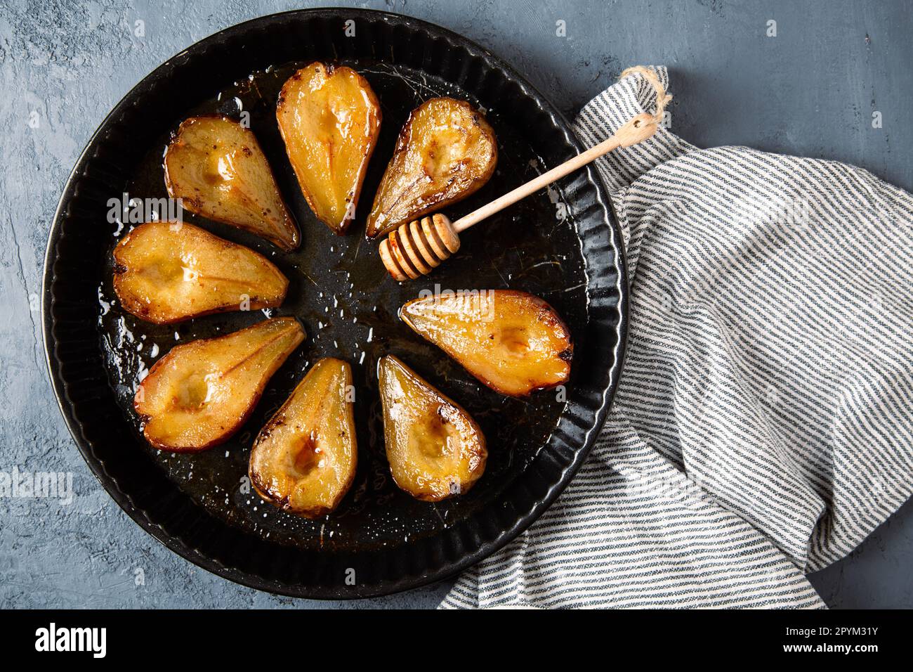 Poires cuites au miel, vinaigrette Modena et cannelle, et une immersion au miel dans une plaque de cuisson ronde sur fond de cocotte bleu grisâtre Banque D'Images