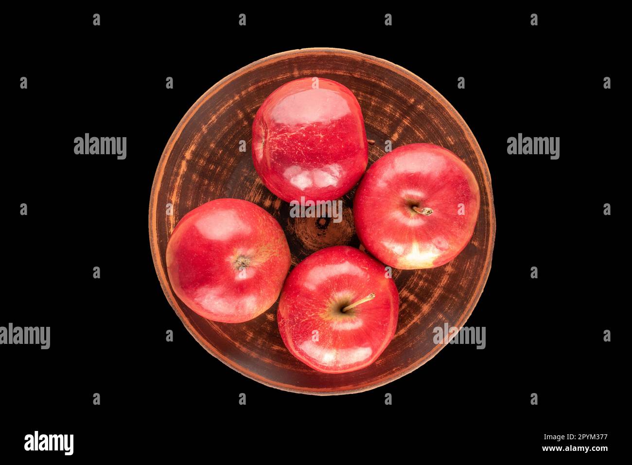 Quatre pommes rouges dans une assiette en argile sur fond noir, vue de dessus. Banque D'Images