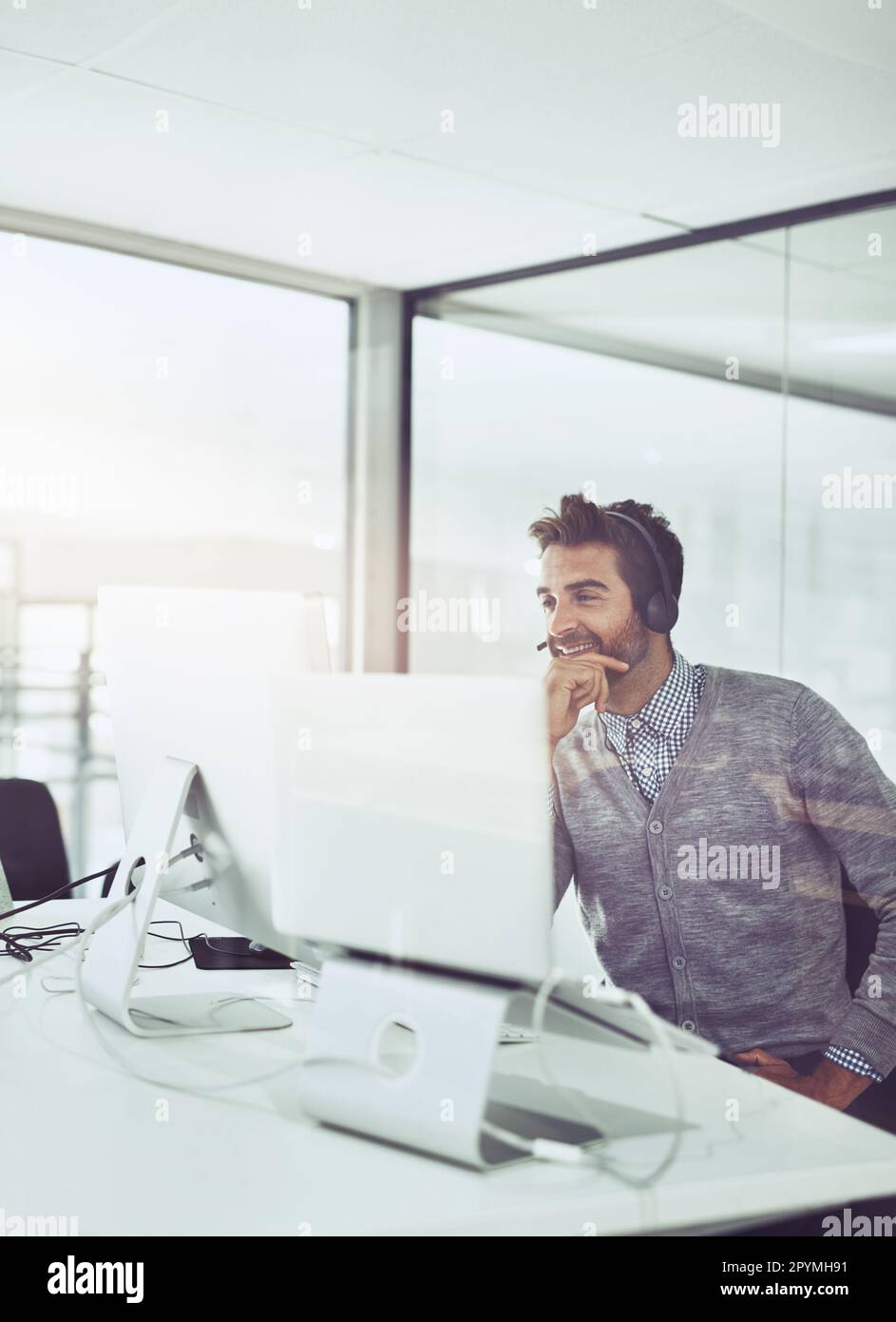Prendre soin des clients. Prise de vue en grand angle d'un jeune homme d'affaires charmant portant un casque tout en étant assis à son bureau. Banque D'Images