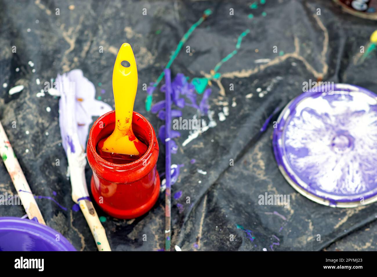 une boîte de peinture rouge est montée sur une toile noire avec des taches de peinture, il y a une brosse avec une poignée jaune dans la boîte pour peindre la surface sur la rue Banque D'Images