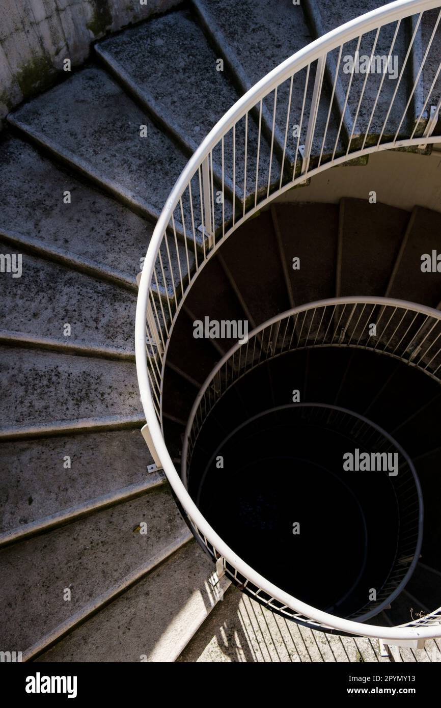 Un escalier en spirale en béton et en métal descendant dans un puits d'escalier sombre. Banque D'Images