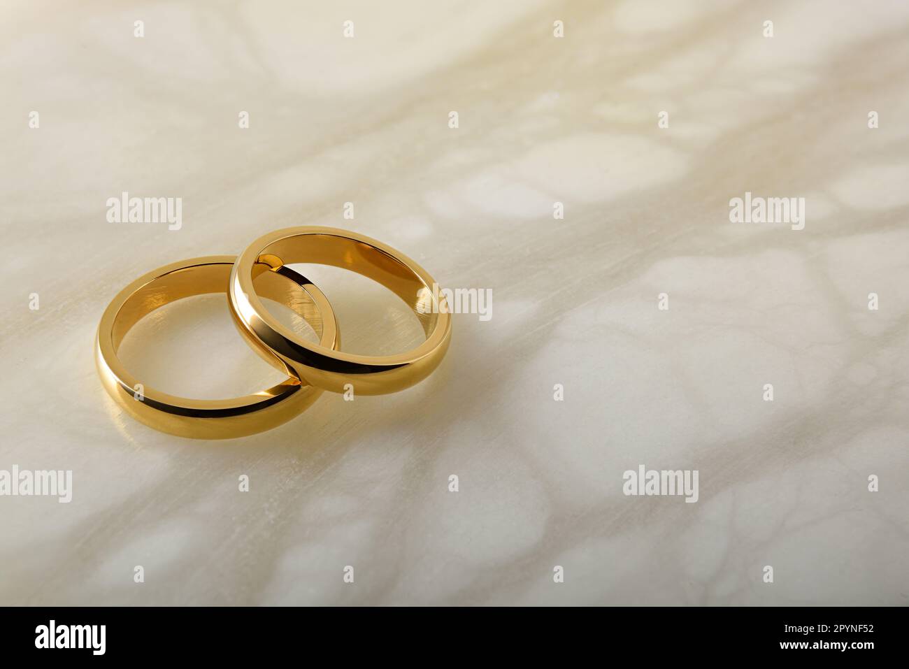 Détail de deux anneaux de mariage dorés l'un sur l'autre sur le marbre blanc. Vue en hauteur du dessus. Banque D'Images