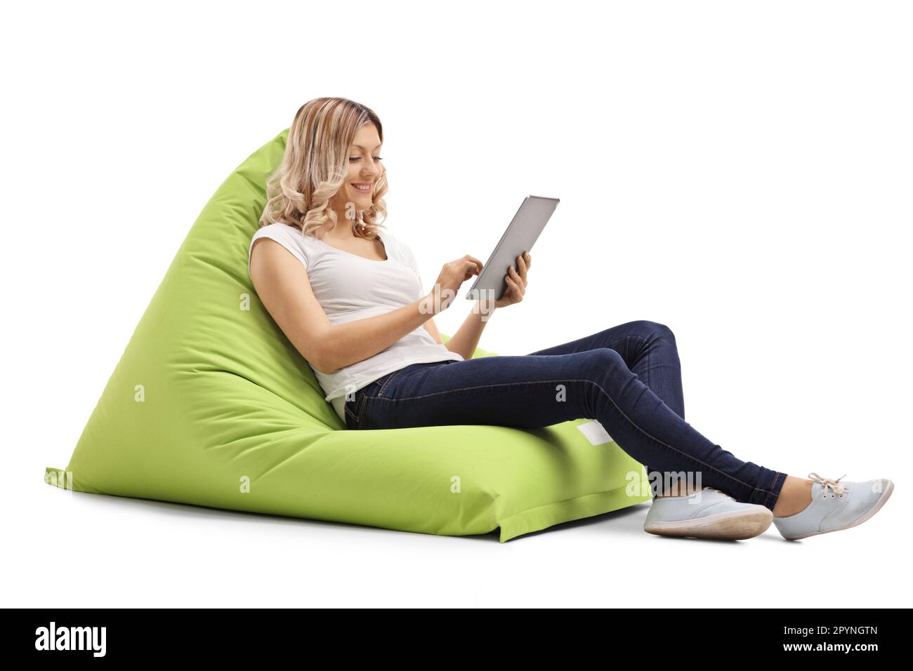 Jeune femme sur une chaise de sac de haricot utilisant un comprimé numérique isolé sur fond blanc Banque D'Images Jeune femme sur une chaise de sac de haricot utilisant un comprimé numérique isolé sur fond blanc Banque D'Images