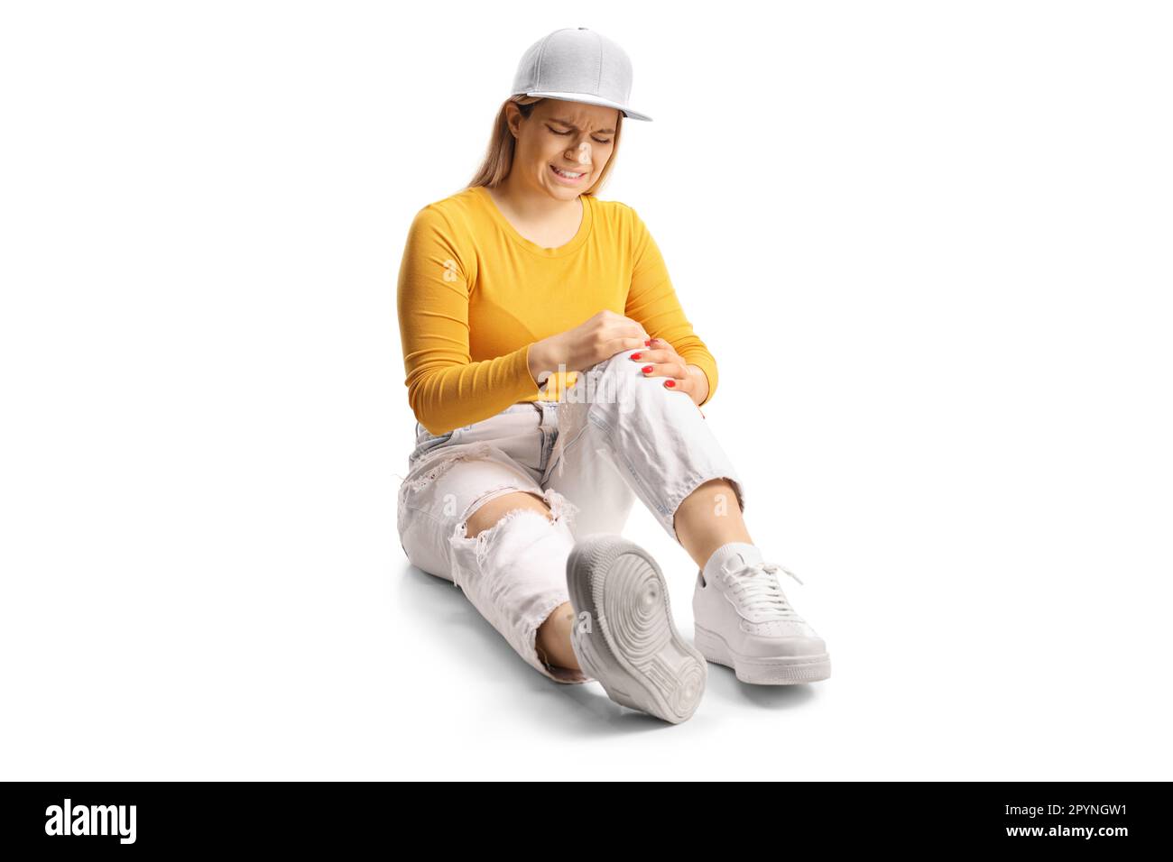 Jeune femme assise sur le sol et tenant son genou douloureux isolé sur fond blanc Banque D'Images