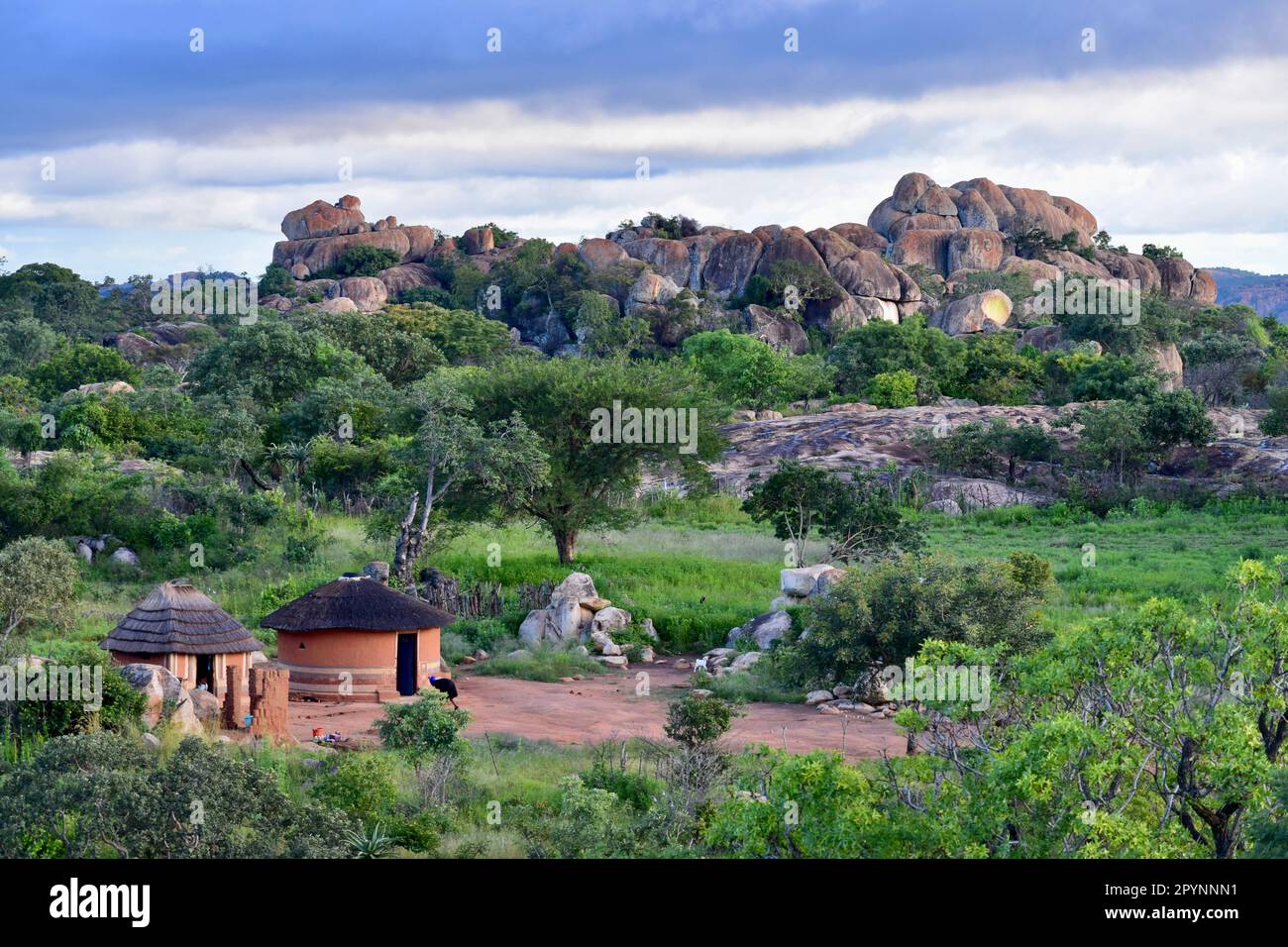 Paysage avec des huttes traditionnelles et femme balayant et des formations rocheuses d'équilibre naturel au Zimbabwe Banque D'Images