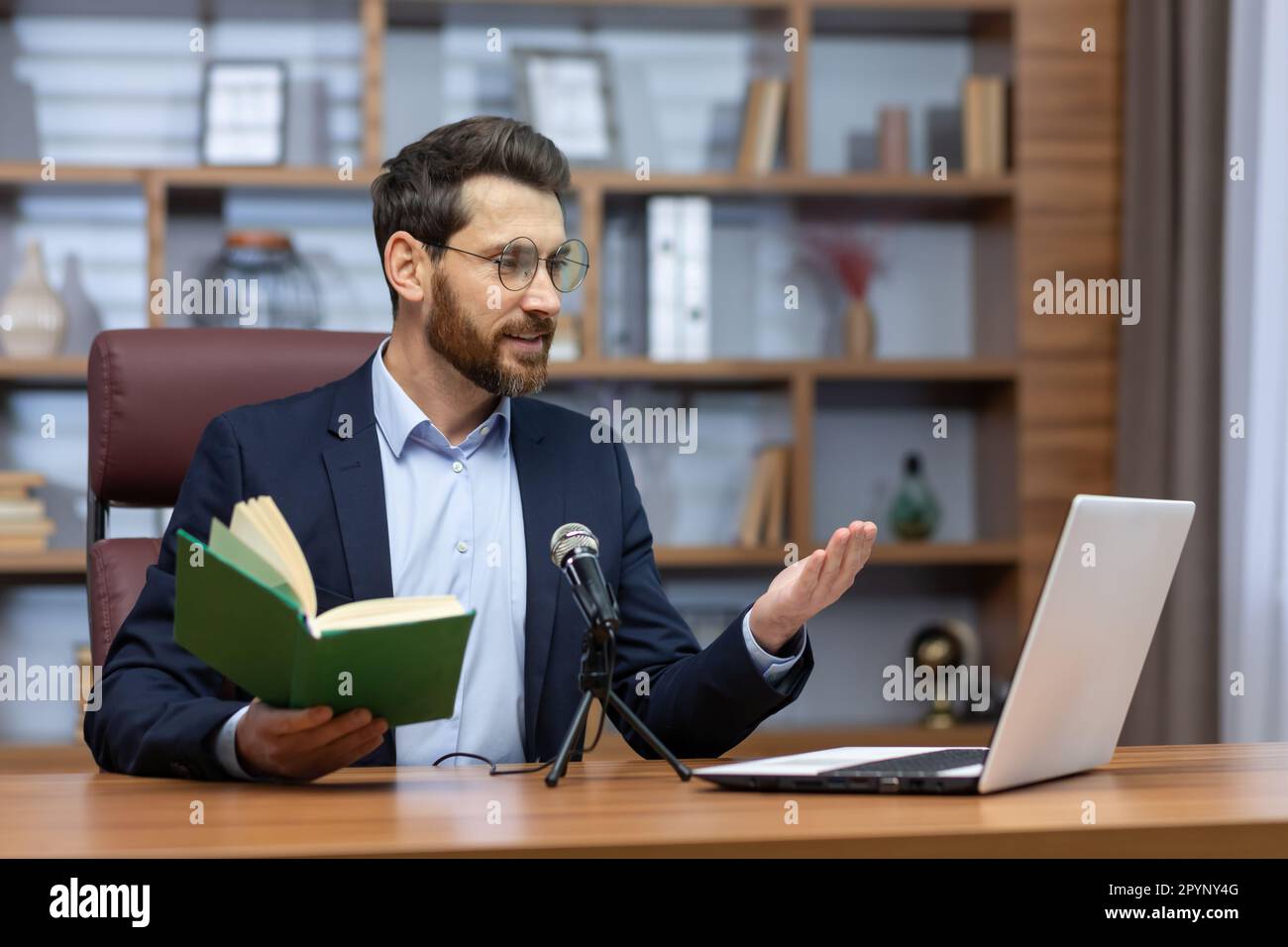 Jeune homme pasteur d'une église, la communauté est assise dans le bureau avec un ordinateur portable et un microphone et lit un sermon. Prières en ligne de la Bible. S'adresse aux croyants et aux paroissiens par appel vidéo. Banque D'Images