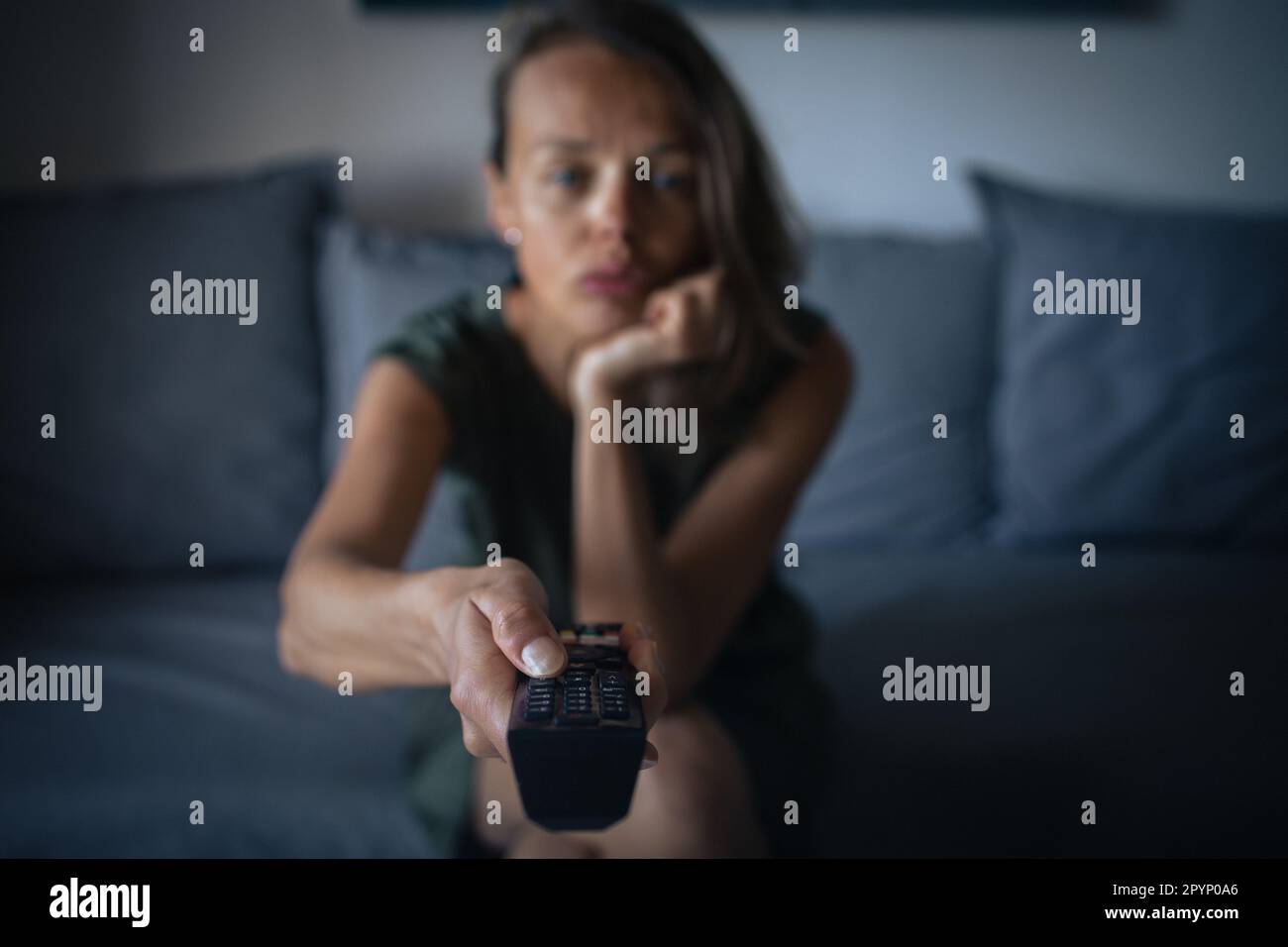 Jolie jeune femme assise sur le canapé à l'intérieur à la maison et regardant la télévision Banque D'Images