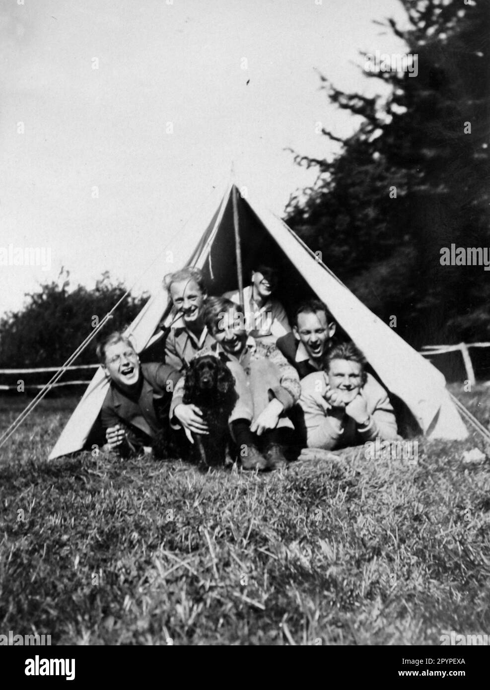 Un grand groupe d'hommes et un chien dans une tente à deux hommes, connue sous le nom de tente de randonnée, c1930. À partir d'un album unique de photographies, compilé par K.W. Parkhurst, d'un camp de campagne à Bolney (une communauté agricole), West Sussex, Angleterre, qui, entre 1928 et 1930, était une destination régulière pour un groupe de jeunes hommes dont M. Parkhurst. C'était pendant la période de la Grande Dépression. Banque D'Images