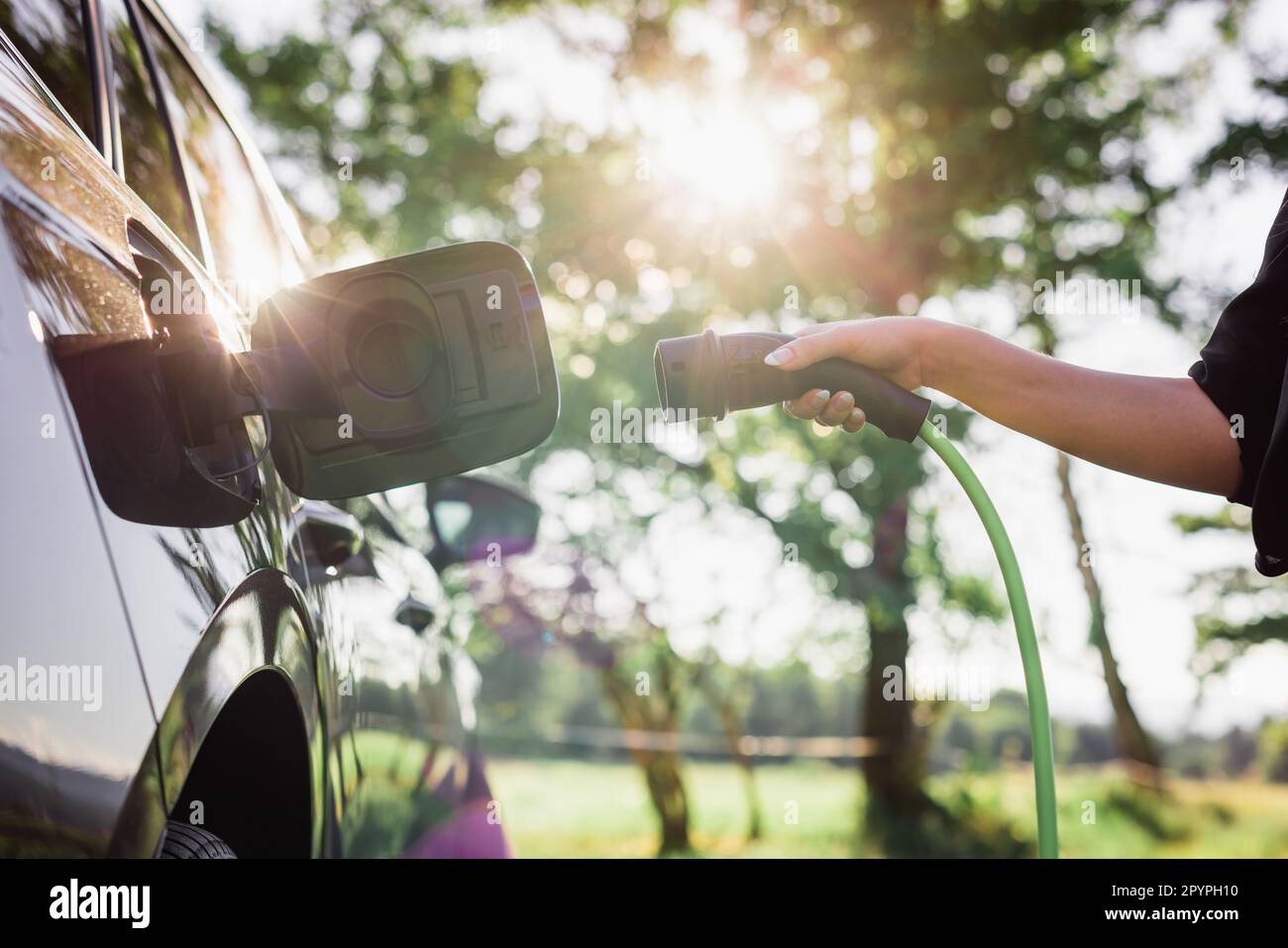 Jeune femme brancher le chargeur dans une voiture électrique noire, concept d'énergie renouvelable Banque D'Images