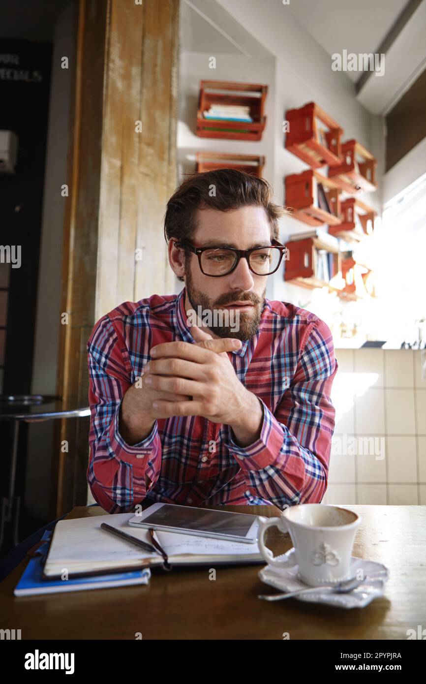 Je ne crois pas qu'il soit en retard pour notre réunion... un jeune homme assis dans un café avec sa tablette et son journal en face de lui. Banque D'Images