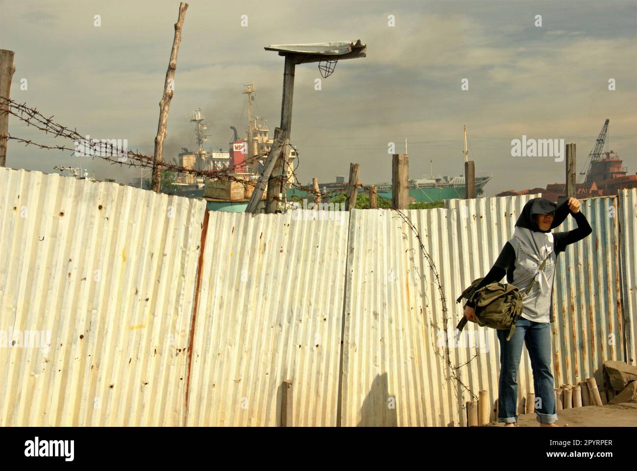 Un travailleur d'ONG est photographié devant une clôture qui sépare une cour de démolition de navires d'une route étroite et d'un étang près du village côtier de Marunda à Cilincing, Jakarta, Indonésie. Banque D'Images