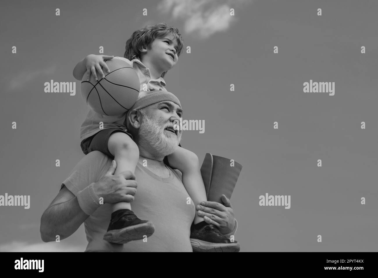 Préparation à l'entraînement matinal dans le parc.Joyeux petit garçon souriant sur l'épaule grand-père regardant l'appareil photo.L'enfant est assis sur les épaules de son grand-père. Banque D'Images