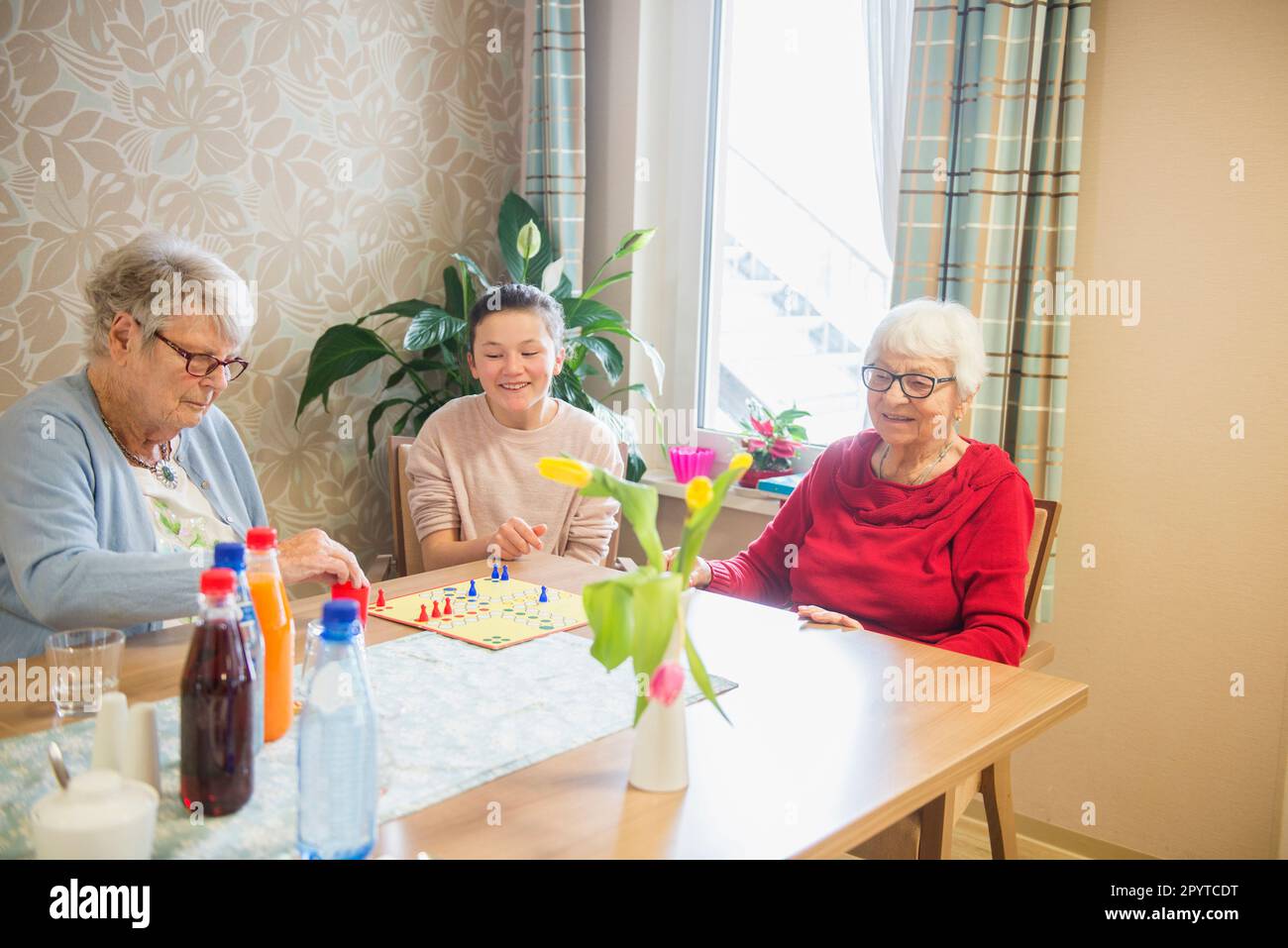Fille jouant à un jeu de société avec des femmes âgées dans la maison de repos Banque D'Images