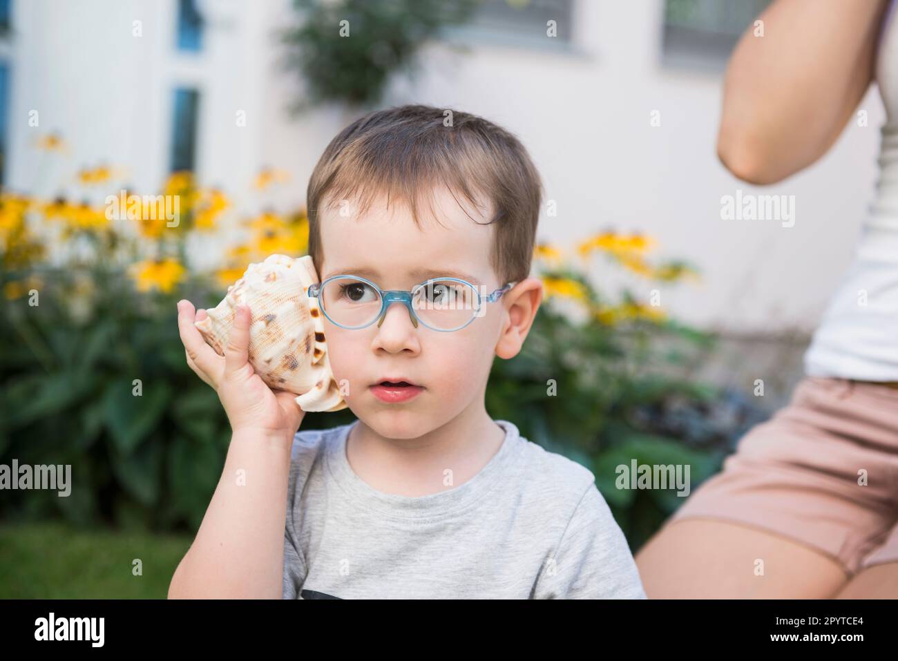 Garçon à l'écoute de seashell à l'extérieur de sa maison, Bavière, Allemagne Banque D'Images