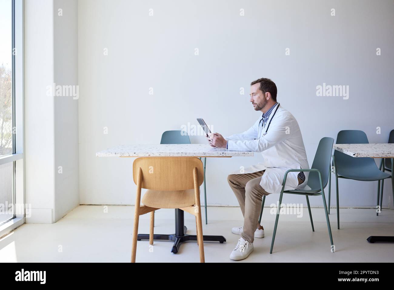 Vue latérale d'un médecin de sexe masculin utilisant une tablette PC tout en étant assis sur une chaise Banque D'Images