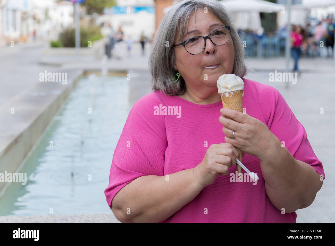femme aux cheveux blancs qui mange de la glace devant une fontaine Banque D'Images