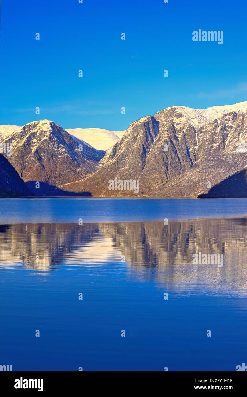 Village de Flam, Norvège - Aurlandsfjord et les montagnes enneigées environnantes se reflètent dans l'eau calme du fjord - ensoleillé avec un ciel bleu clair Banque D'Images