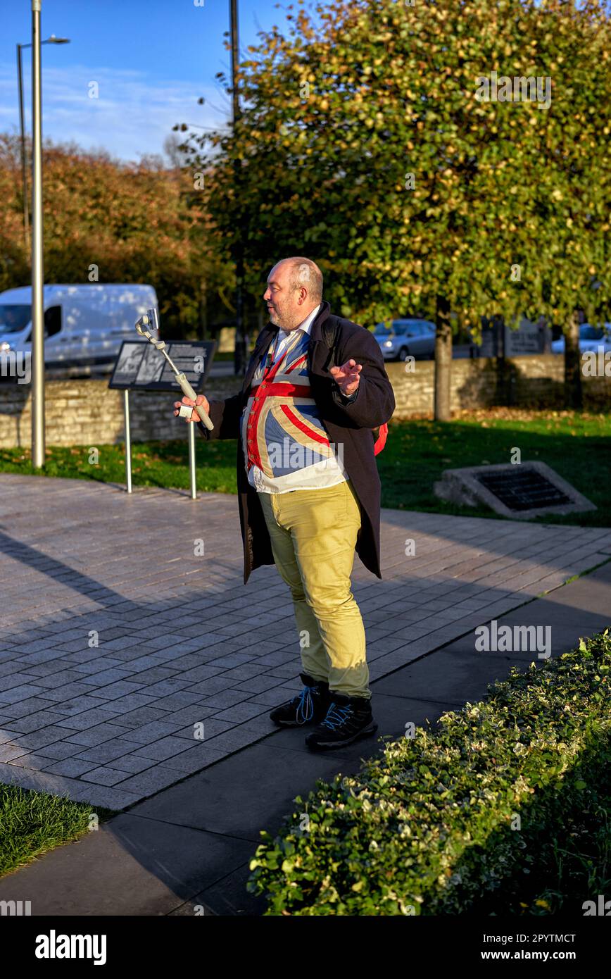 Vlogger et influenceur, homme anglais excentriquement habillé en gilet Union Jack et pantalon jaune tout en filmant en extérieur. Angleterre Royaume-Uni Banque D'Images