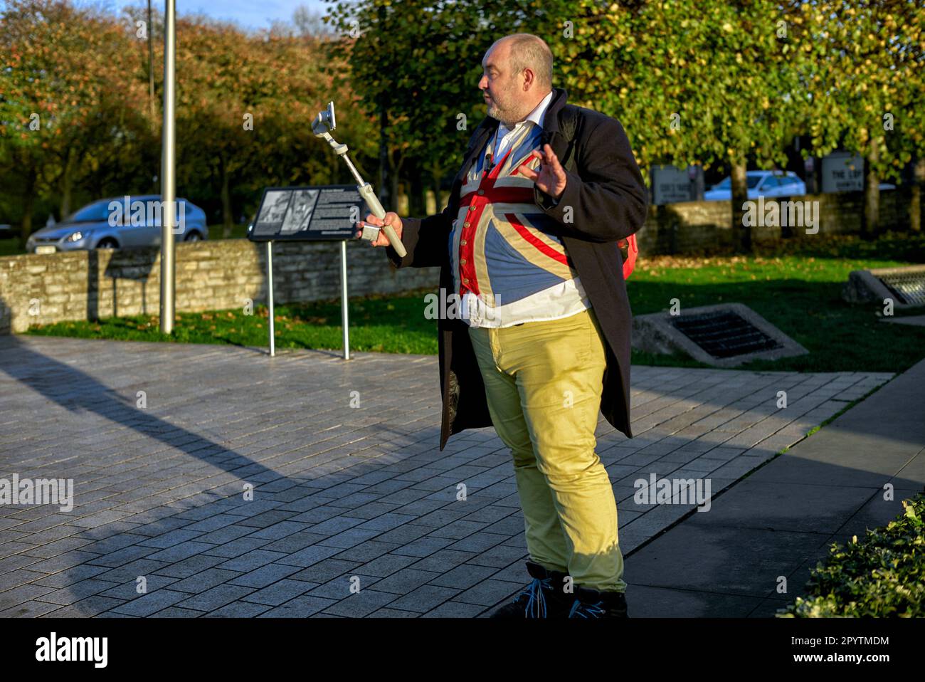 Vlogger et influenceur, homme anglais excentriquement habillé en gilet Union Jack et pantalon jaune tout en filmant en extérieur. Angleterre Royaume-Uni Banque D'Images