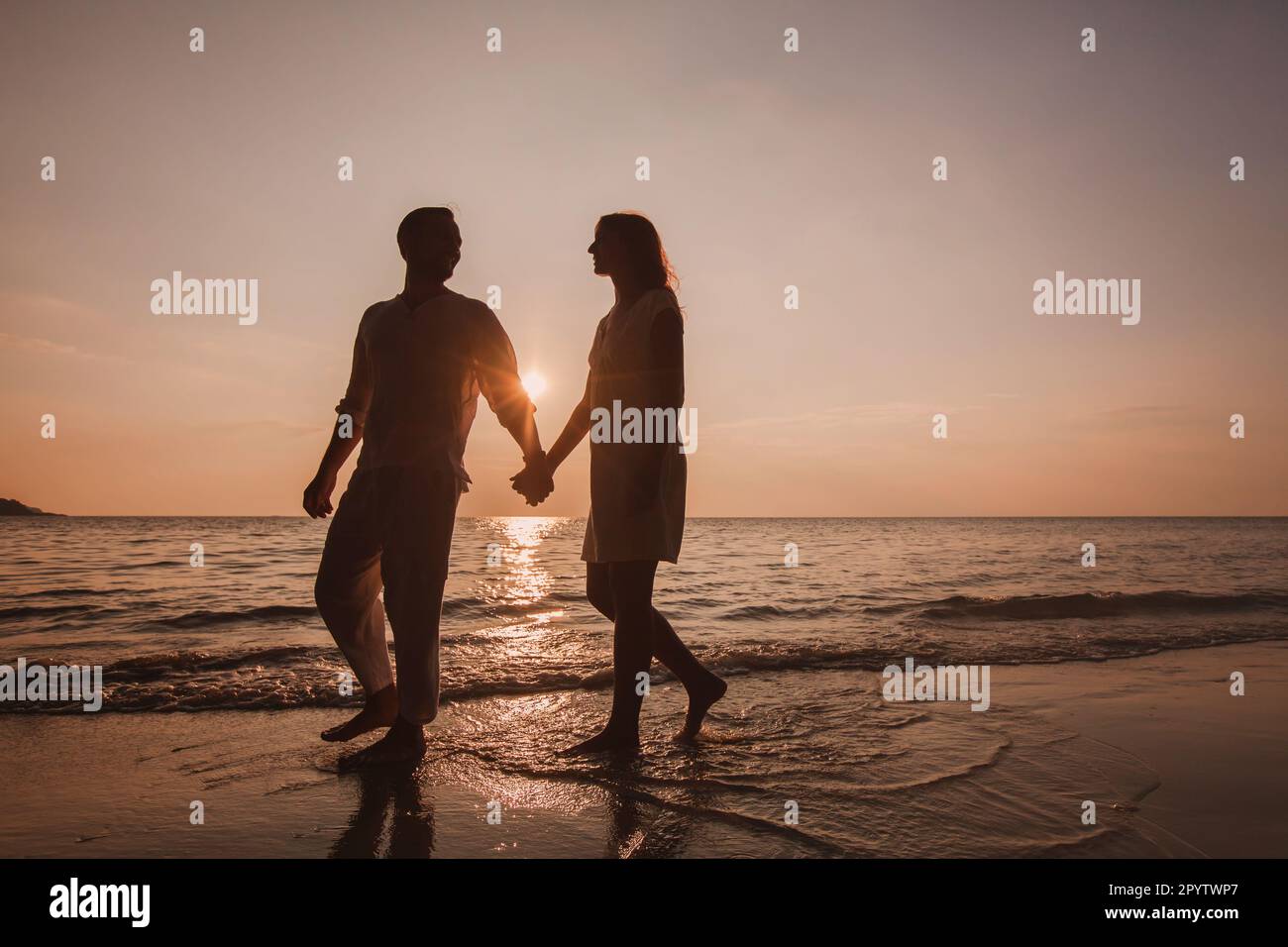 lune de miel, silhouette de couple marchant sur la plage au coucher du soleil et tenant les mains Banque D'Images