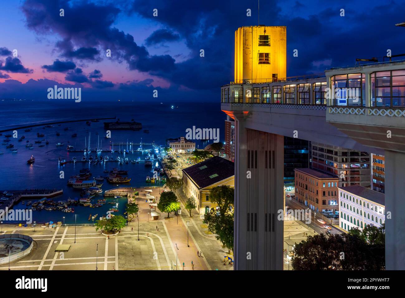 Façade du célèbre ascenseur de Lacerda illuminée la nuit avec la ville et les bateaux en arrière-plan dans la ville de Salvador, Bahia, Brésil Banque D'Images