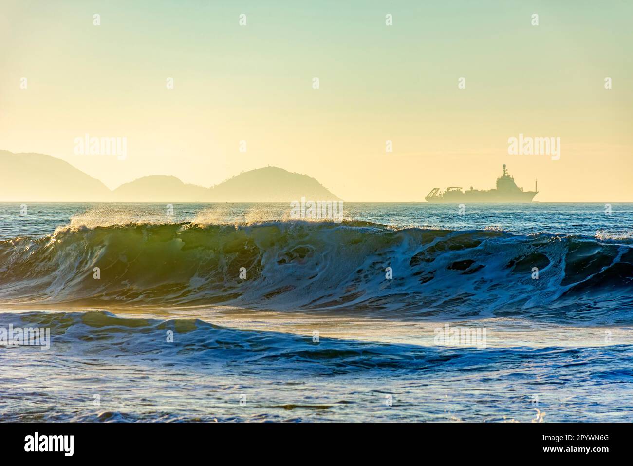 Vagues se brisant sur la plage au lever du soleil avec un bateau traversant l'horizon et les montagnes en arrière-plan., Brésil Banque D'Images