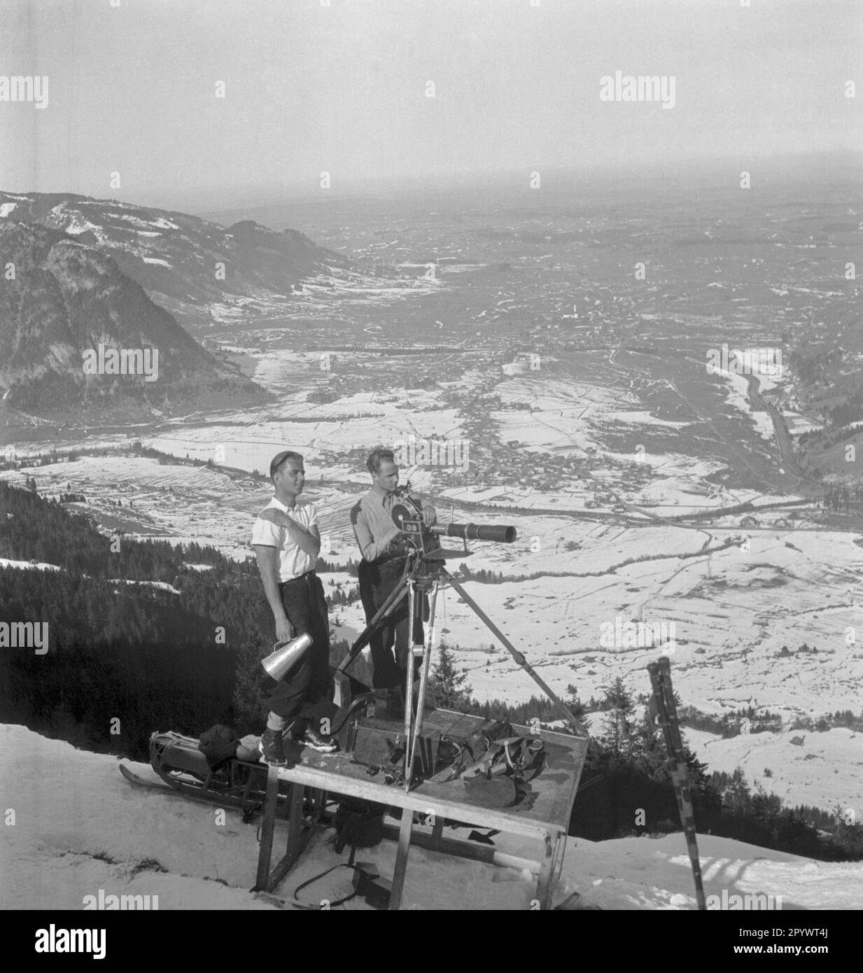 Deux caméramans attendent sur leur élévateur pendant une pause de tir. En arrière-plan, les contreforts des Alpes. Les films datent probablement de la mi-1930s et sont liés aux Jeux Olympiques d'hiver de 1936 à Garmisch-Partenkirchen. Banque D'Images