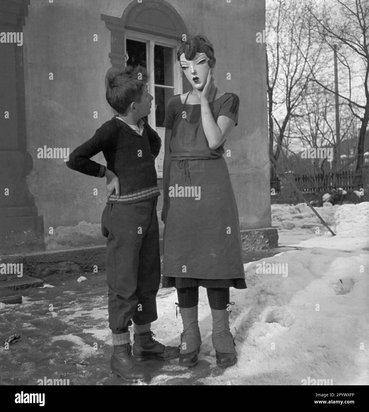 Un garçon et une jeune fille tenant un masque de femme sculpté à la main et peint devant son visage, se tiennent devant une maison en haute-Bavière (photo non datée). Banque D'Images