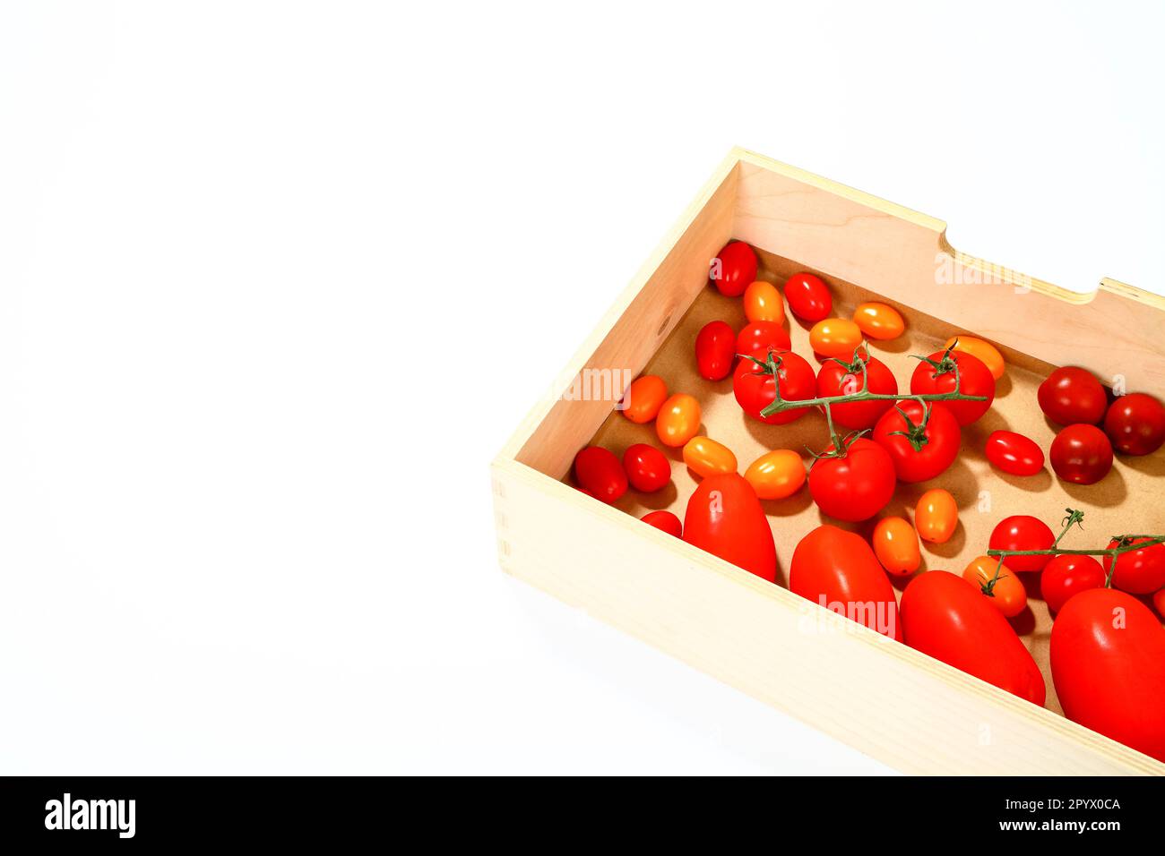 Tomates prune et cerise dans une boîte en bois isolée sur fond blanc avec espace de copie Banque D'Images