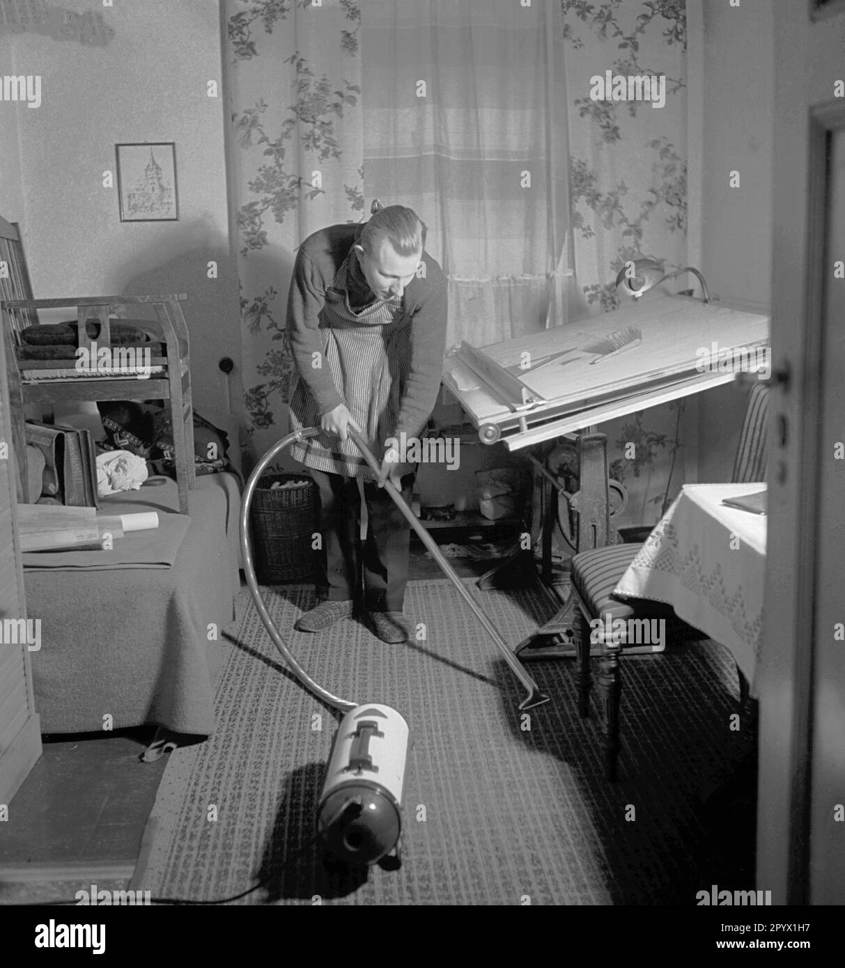 « Un homme passant l'aspirateur sur le tapis dans l'étude. Scène de la série ''nous travaillons ensemble'. Le photographe accompagne les couples dans leurs occupations respectives. » Banque D'Images