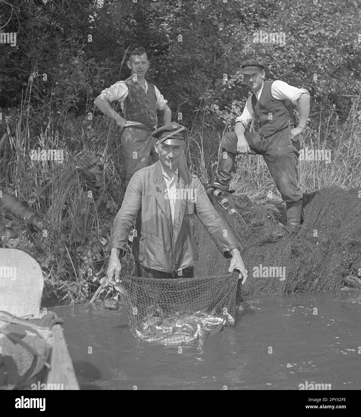 Le chasseur d'un manoir présente au photographe sa prise. Le filet est plein de poisson. Deux autres hommes se tiennent derrière lui. Photo non datée, probablement sur une ferme dans la province de Pomerania en 1930s. Banque D'Images