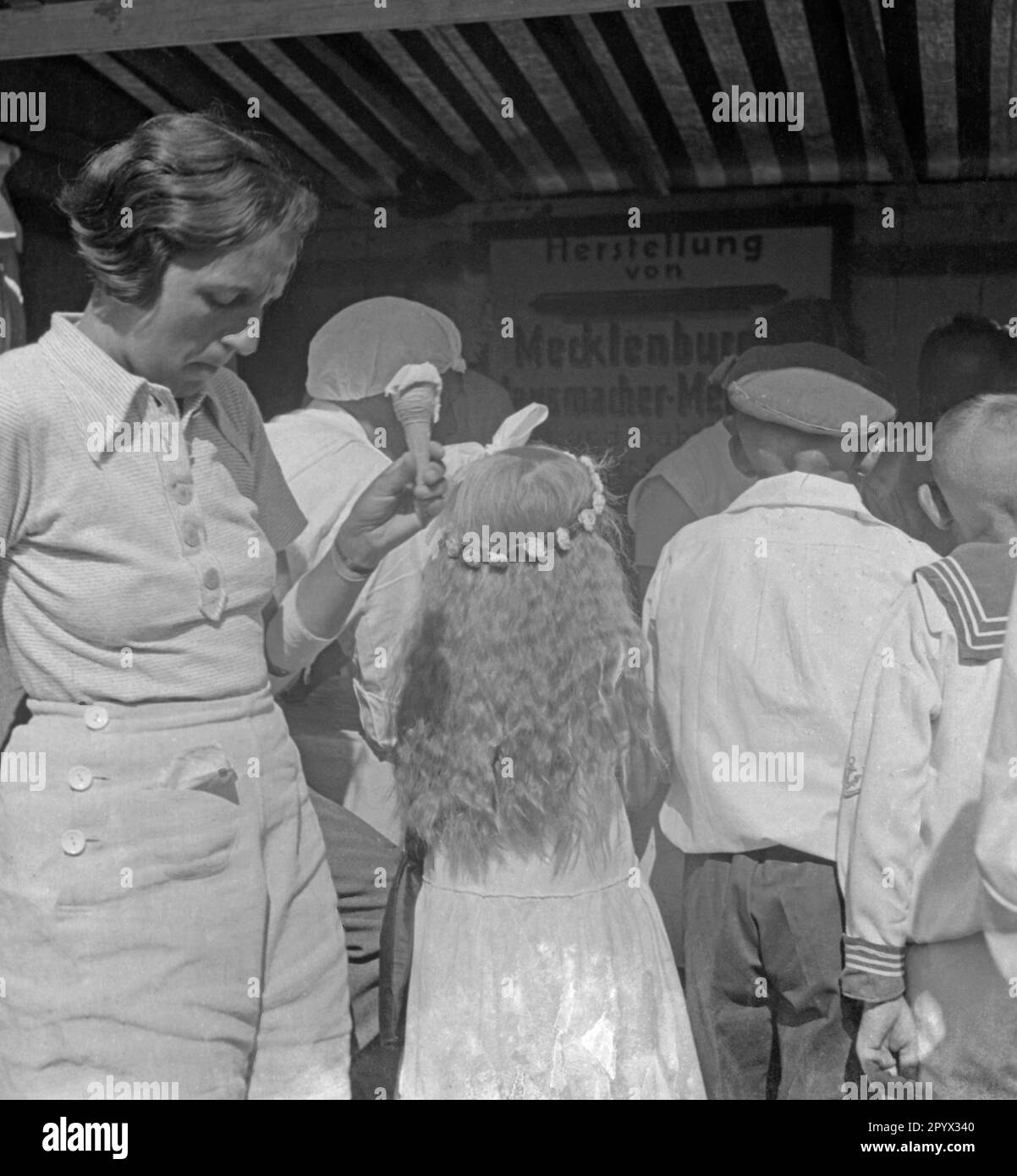 Une femme tient un cône de glace dans sa main, juste à côté d'elle est une petite fille avec une couronne de fleur dans ses cheveux (balle non datée). Banque D'Images