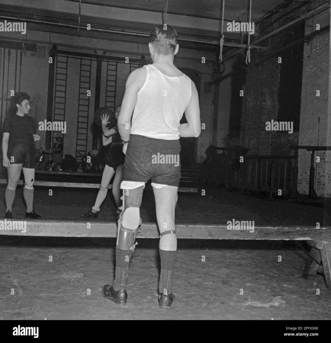 Photo non datée des amputés de jambes lors d'un exercice de réadaptation dans une salle de sport à Berlin, probablement Berlin-Ouest, 1950. Les deux femmes et un homme dans les vêtements de sport ont des jambes artificielles, et se lancent un ballon de médecine pendant un exercice de renforcement. Banque D'Images
