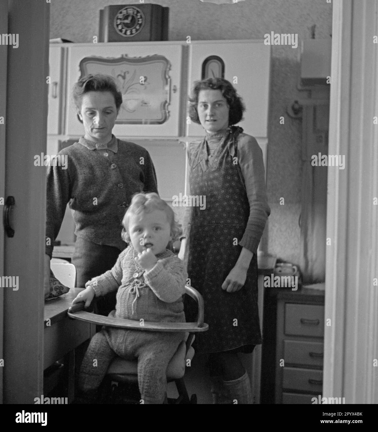 Photo sans date d'une veuve d'un soldat allemand tué dans la guerre prise dans une cuisine à manger à Berlin, probablement Berlin-Ouest, 1950. Au premier plan, son enfant s'assoit sur une chaise d'enfant. Banque D'Images