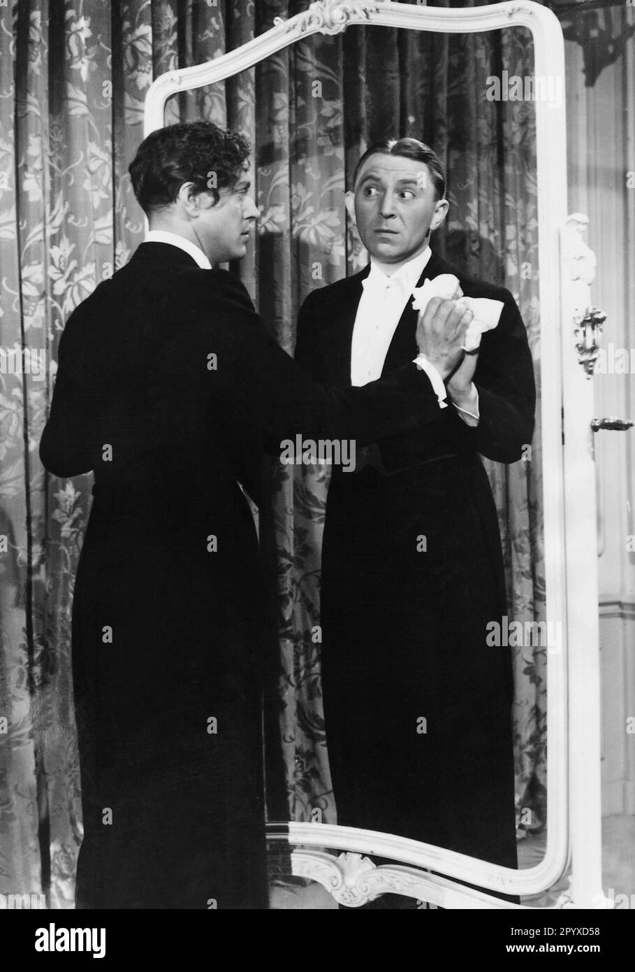 Theo Lingen (à droite) comme maître d'hôtel dans le film "les années de malchance" veut empêcher son maître, Wolf Albach-Retty (à gauche), de remarquer qu'un autre miroir a été brisé. [traduction automatique] Banque D'Images