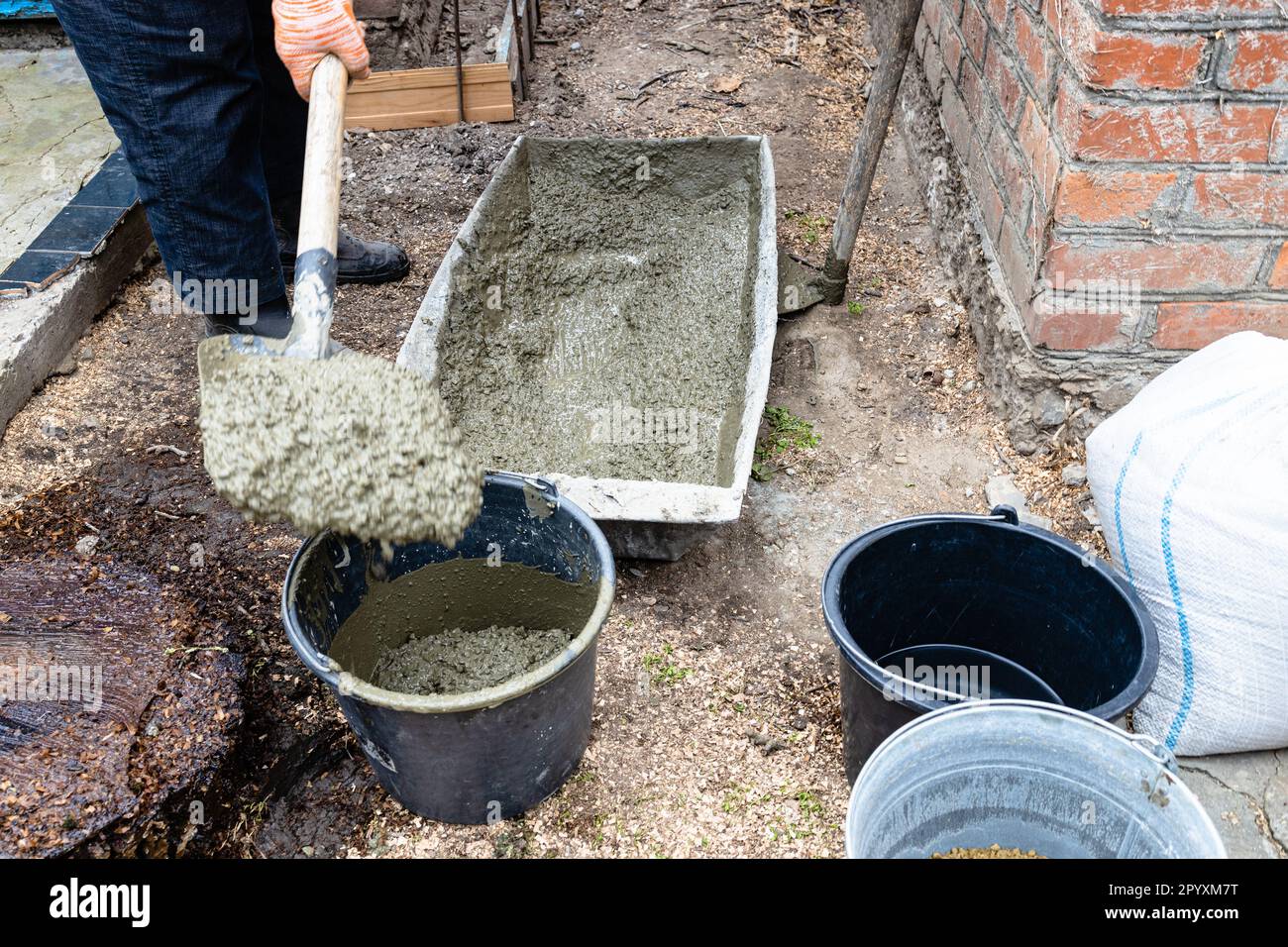 builder met le béton dans un seau avec une pelle dans l'arrière-cour dans le village à l'extérieur Banque D'Images