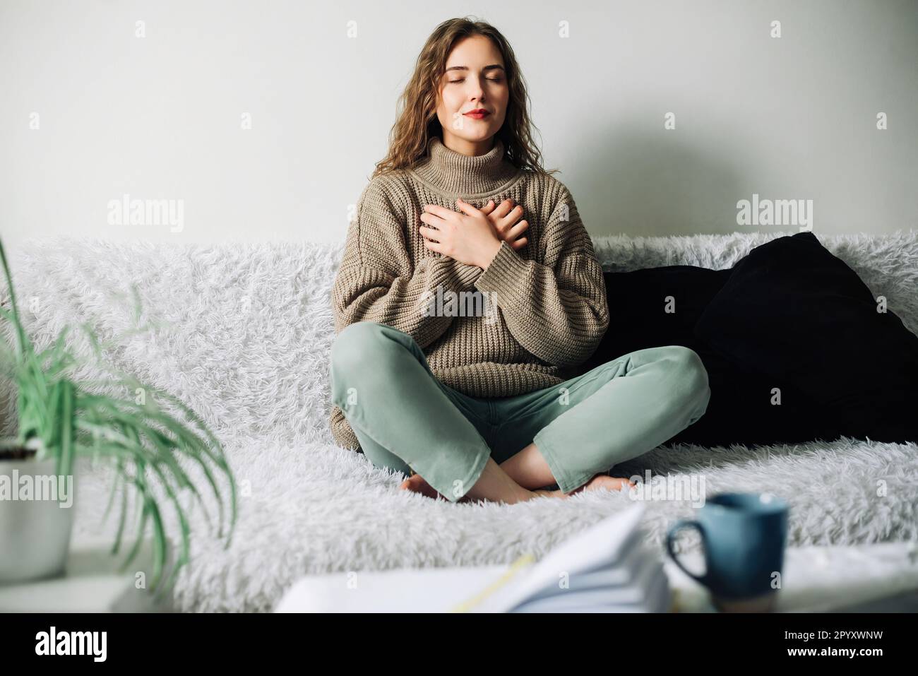 Belle jeune femme au lotus pose sur le lit pratiquant des techniques de respiration de pranayama, trouvant l'équilibre intérieur après une journée stressante Banque D'Images