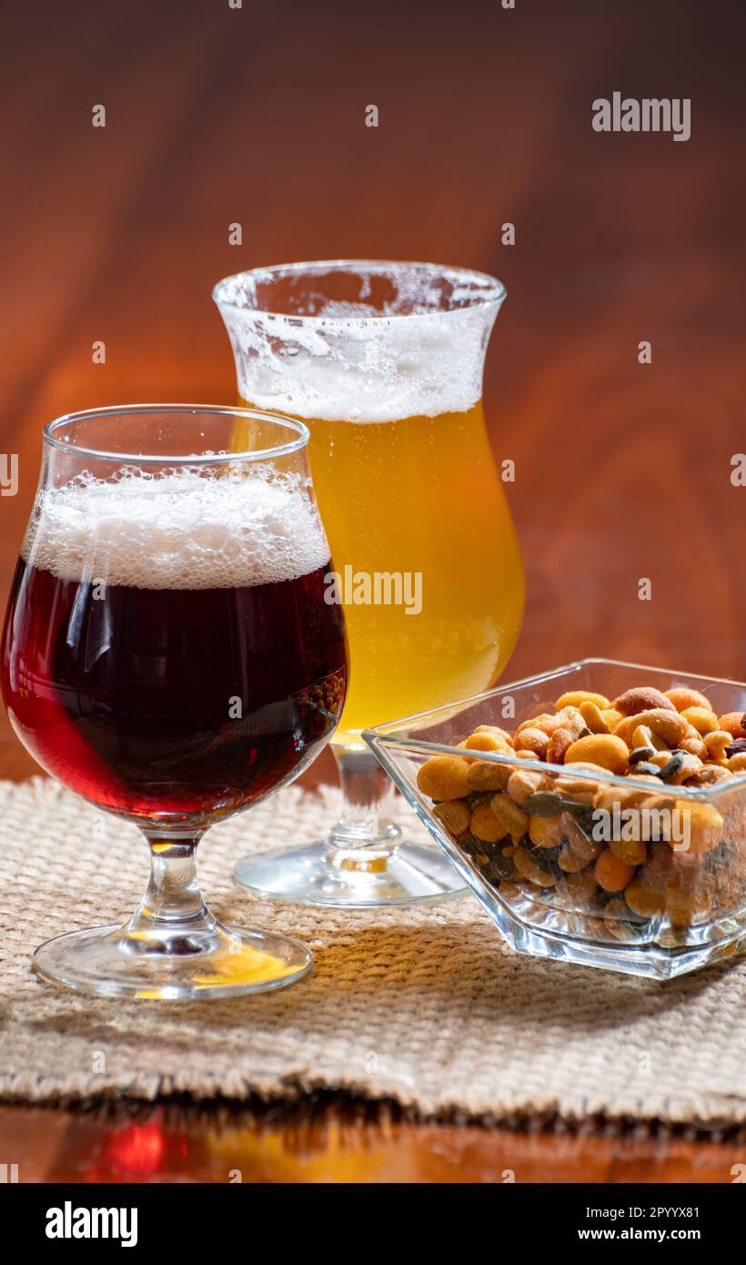 Verres de bière blonde jaune belge et marron foncé faits à l'abbaye servis au bar avec noix de fête, gros plan Banque D'Images