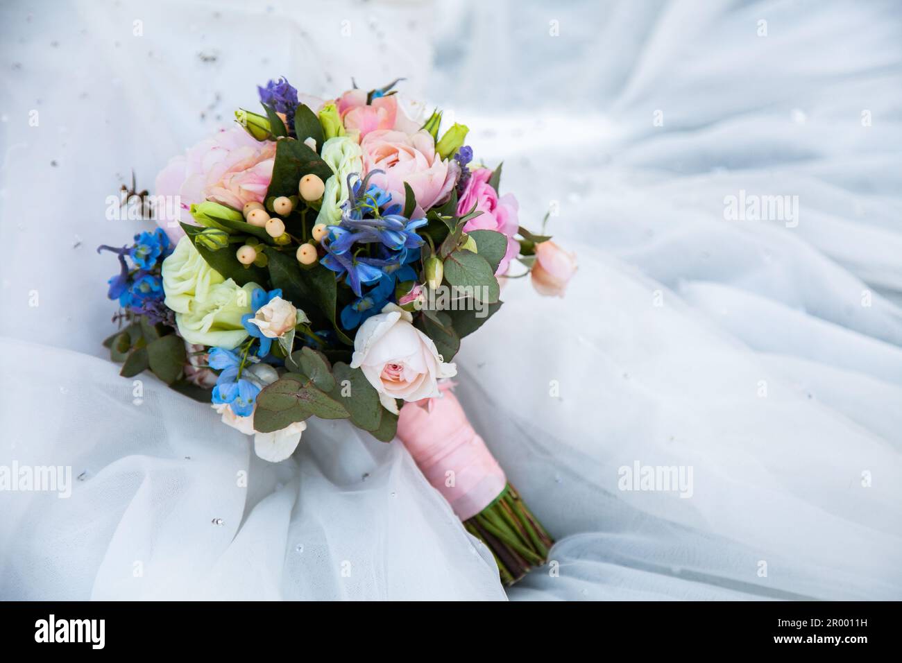 Bouquet de fleurs de mariage avec des feuilles de gomme australienne indigène comme feuillage reposant sur des plis de tissu de robe blanc Banque D'Images