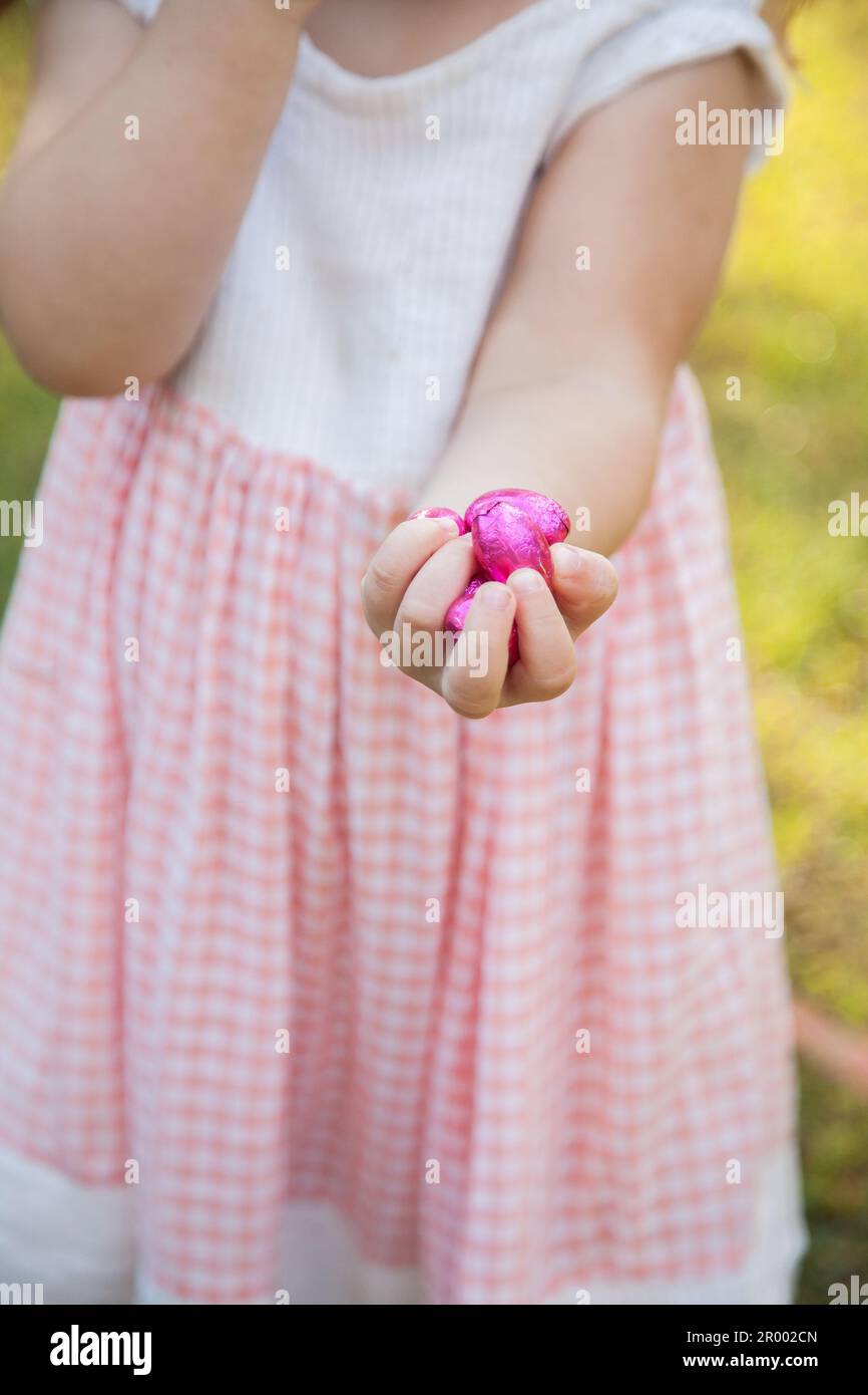 Petite fille avec le poing plein d'oeufs roses de pâques trouvés à la chasse Banque D'Images