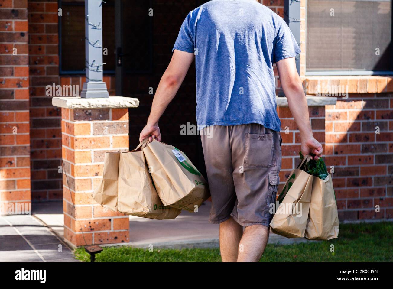 Homme apportant des sacs en papier d'épicerie à la maison de Woolworths avec le magasin d'alimentation hebdomadaire Banque D'Images