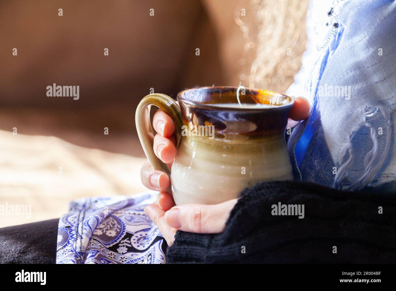 Femme tenant la tasse de boisson chaude assise au soleil venant à l'intérieur en hiver Banque D'Images